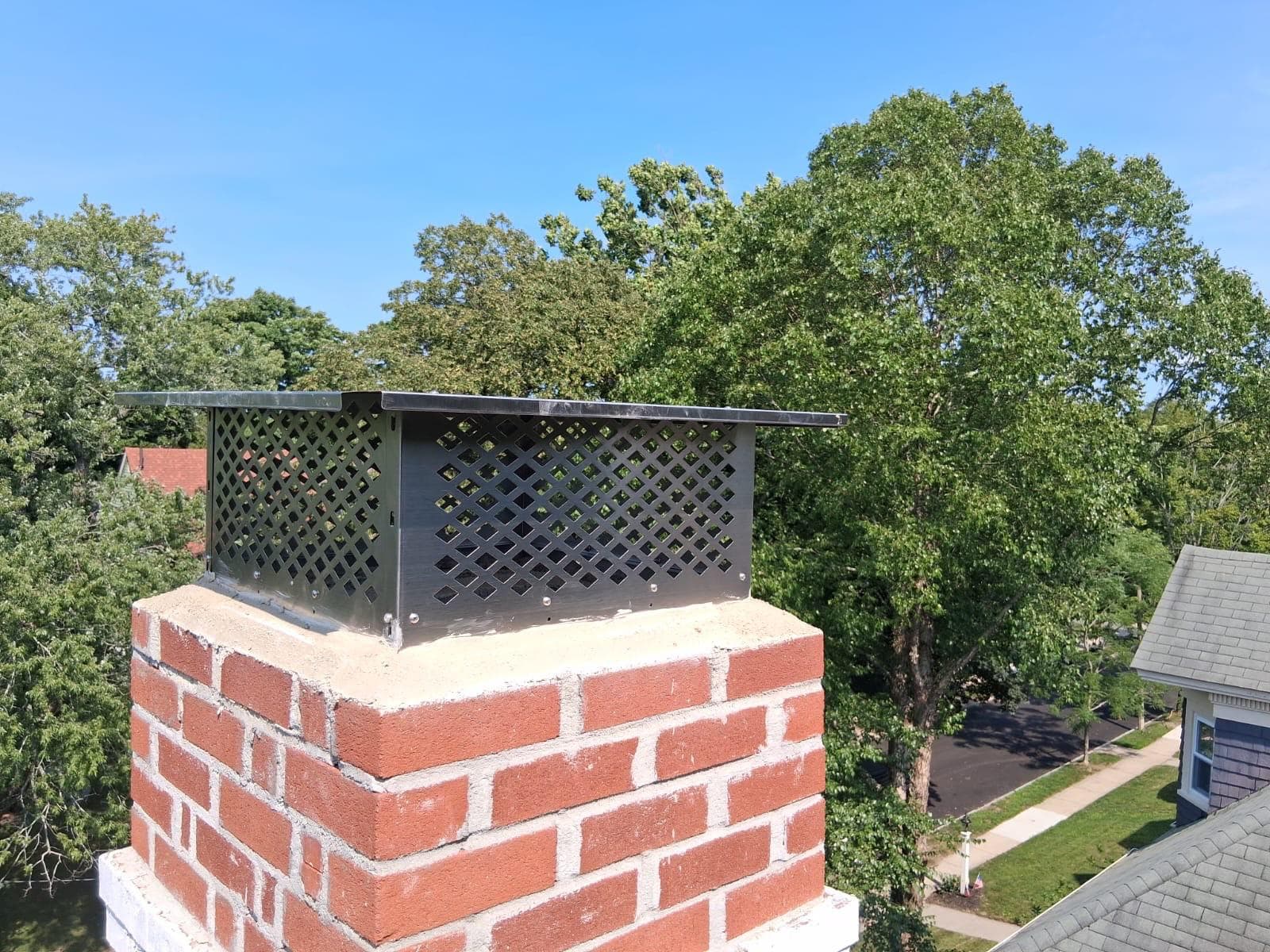 Wide stainless steel lattice chimney cap on a red brick chimney in Greater Boston, Massachusetts