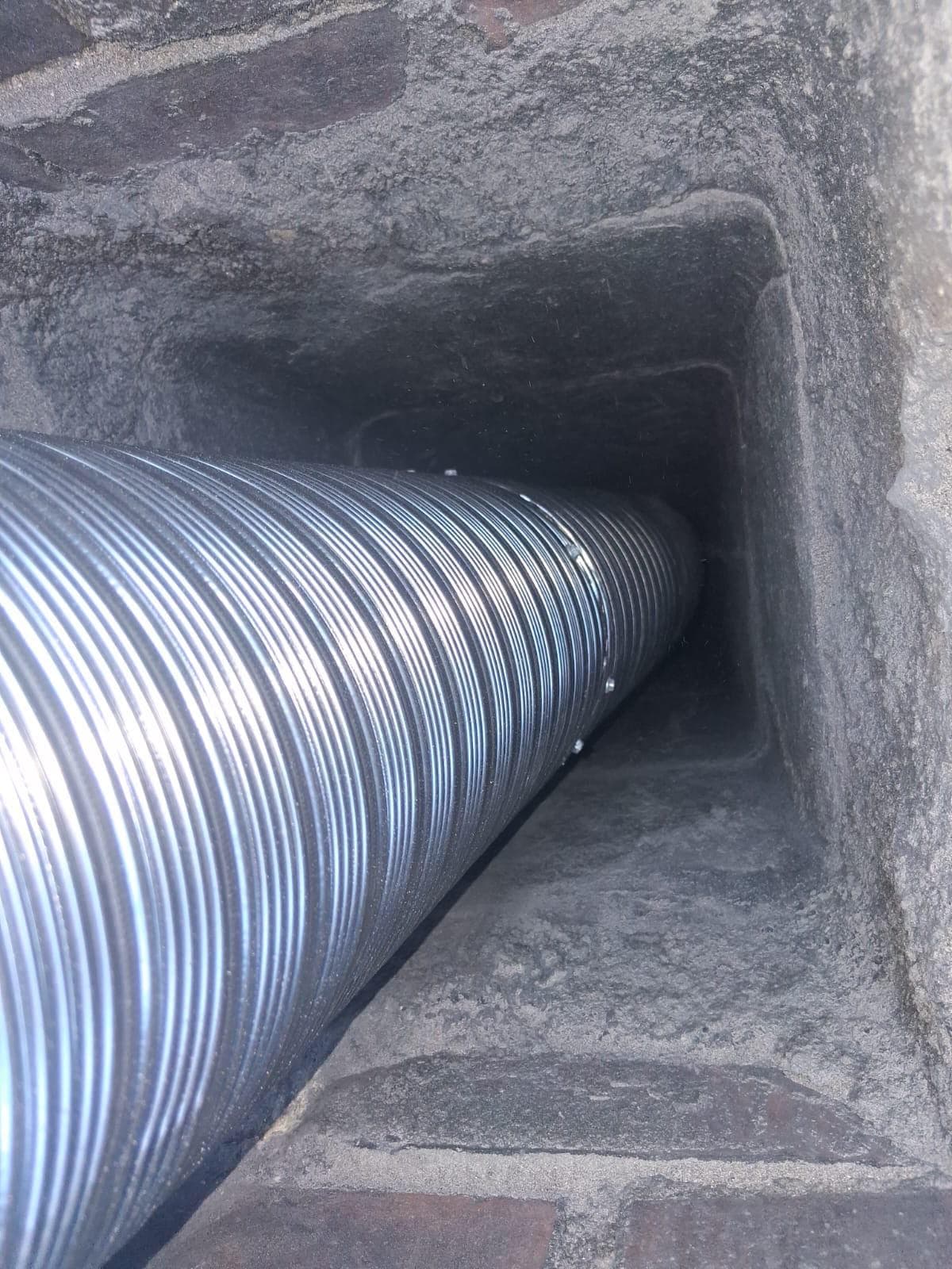 Flexible stainless chimney liner being inserted into a clay flue tile from the top