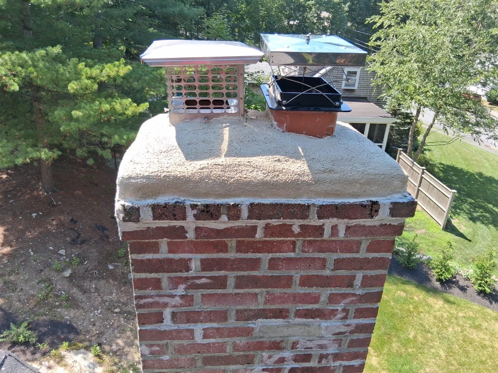 Crown Chimney's finished work — twin stainless caps on a freshly parged crown